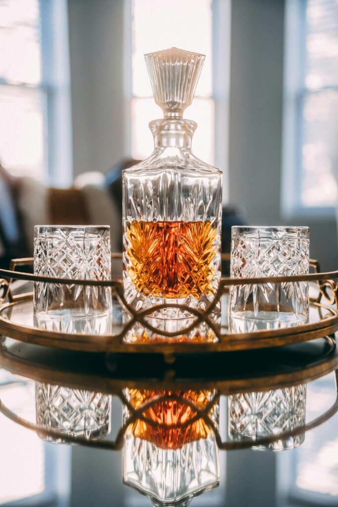Decanter di cristallo con whisky e due bicchieri su un vassoio dorato, luce calda